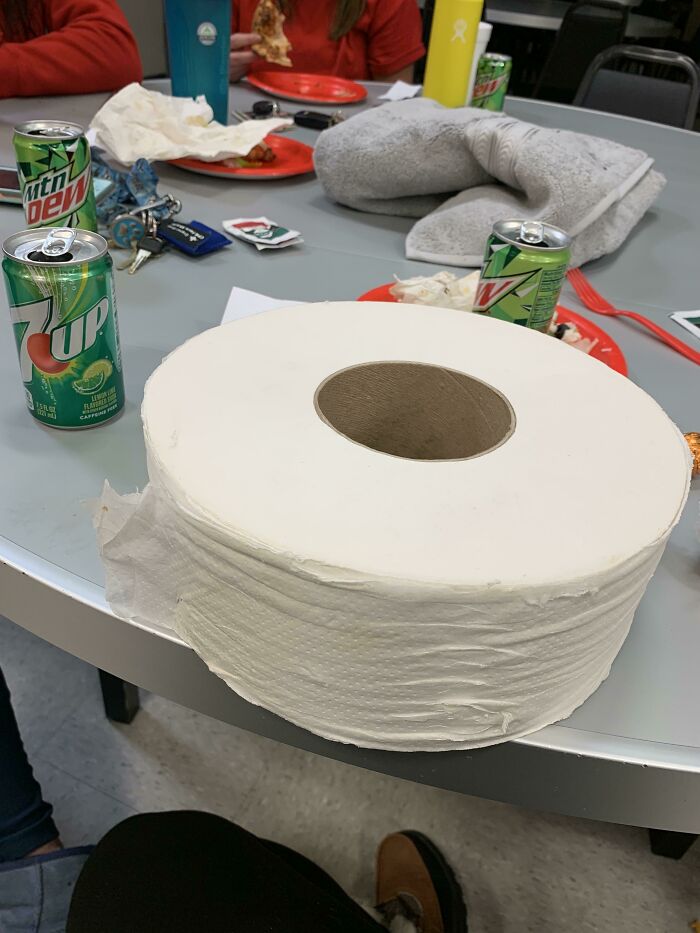 Rollo gigante de papel higiénico en mesa de oficina con refrescos y platos, ejemplo de Secret Santa en desastre laboral.
