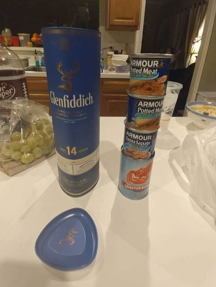 Regalo inesperado de Secret Santa con whisky Glenfiddich y latas de comida apiladas en una cocina.
