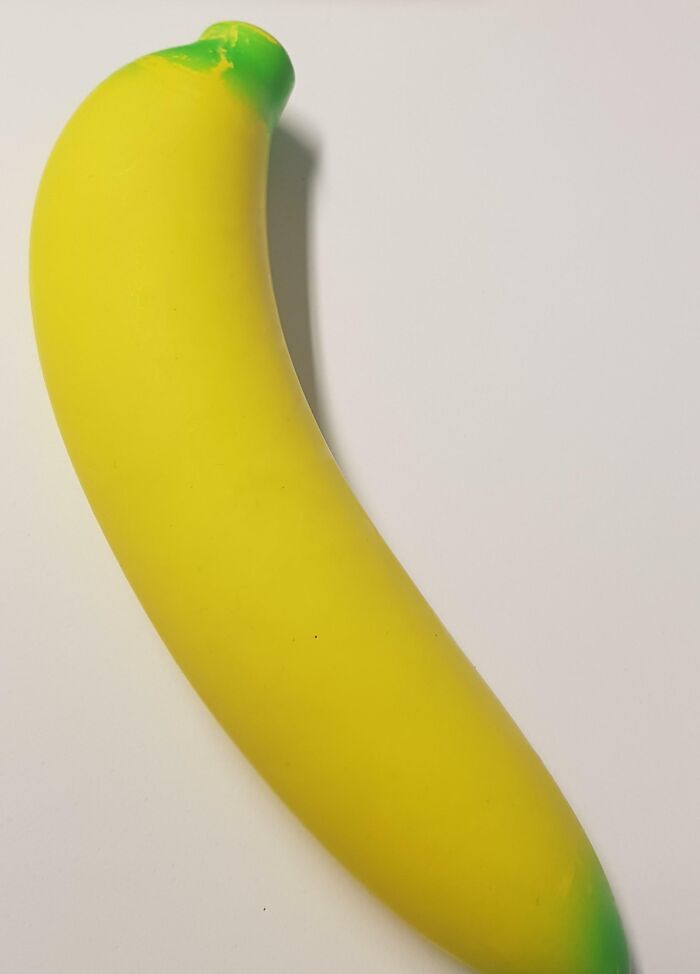 Banana de juguete amarillo con detalles verdes sobre fondo blanco ilustrando historias de Secret Santa en el trabajo.