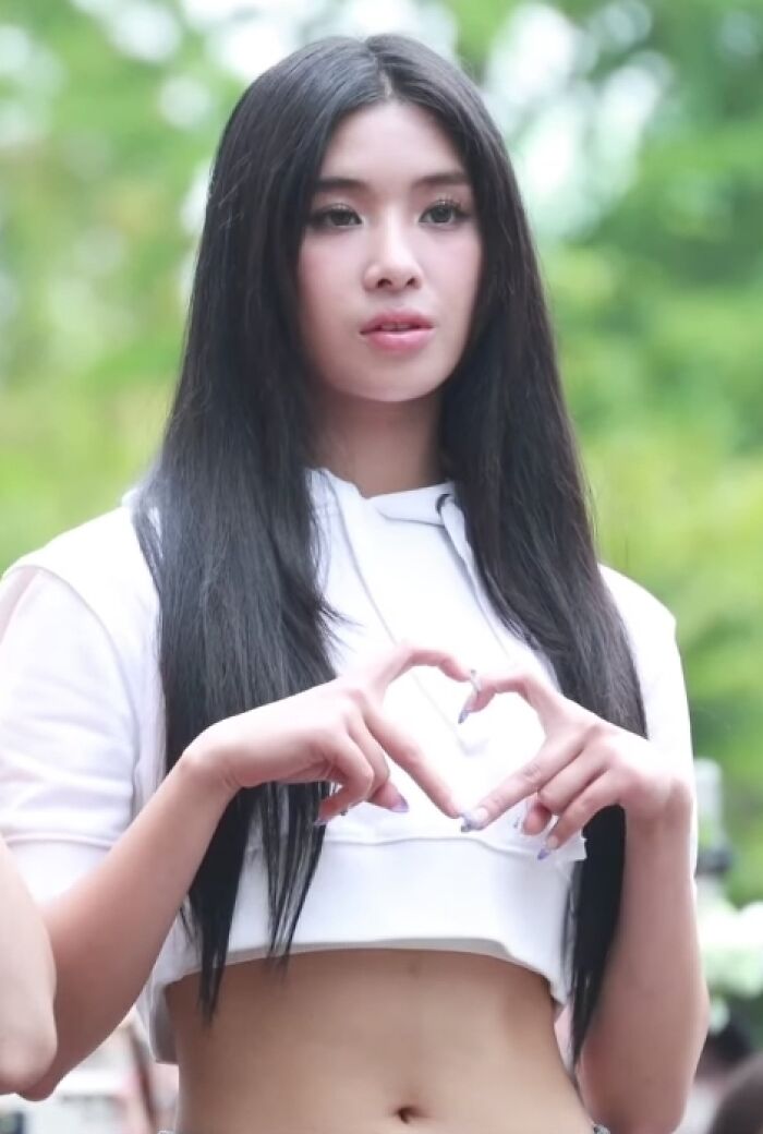 Sophia Laforteza outdoors making a heart shape with hands, wearing a white crop top with long straight hair.