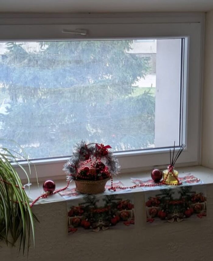 Christmas decorations with red ornaments and tinsel on a windowsill in a sad Lithuanian apartment building.
