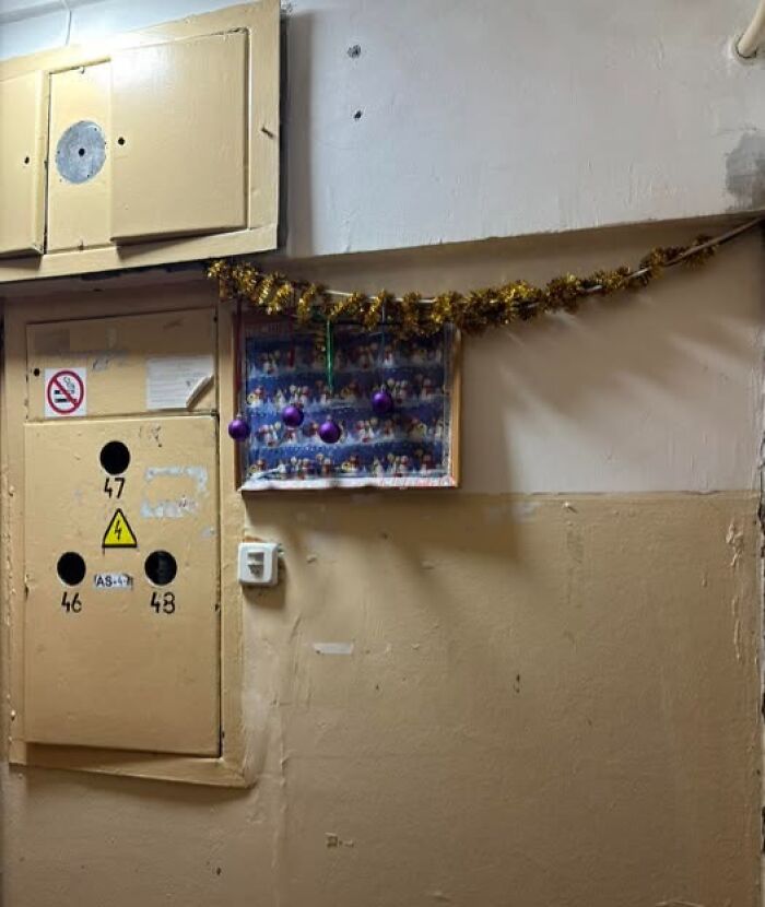 Tacky Christmas decoration with tinsel and baubles on a plain wall in a Lithuanian apartment building hallway.