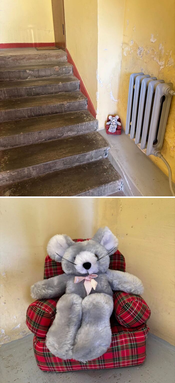 Small plush mouse sitting on a red plaid armchair in a worn Lithuanian apartment building staircase corner.