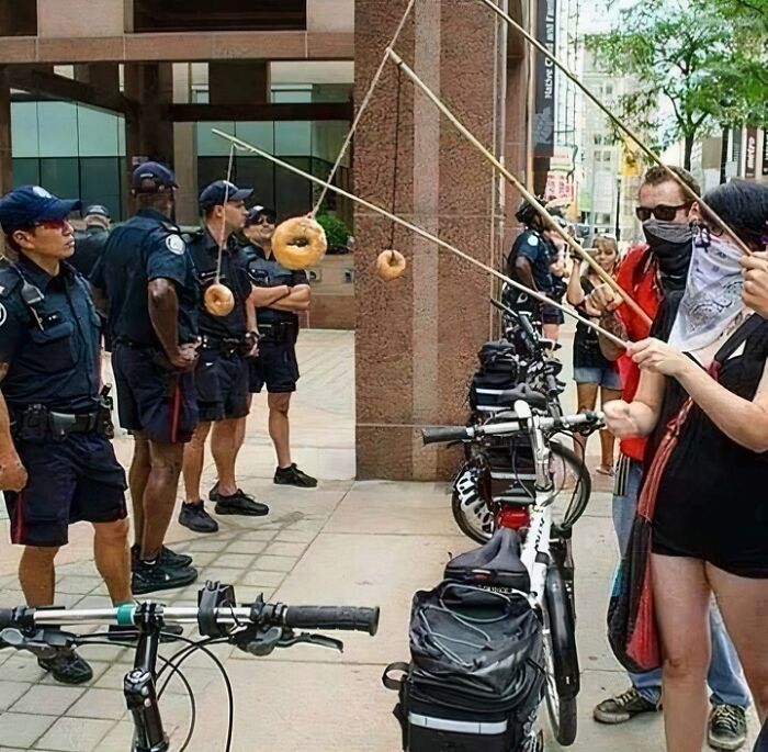 Police officers lined up with donuts hanging on strings while people attempt to eat them hands-free in a humorous scene.