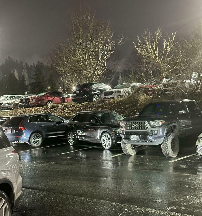 SUV truck parked over two spaces in wet parking lot at night, example of next-level jerks