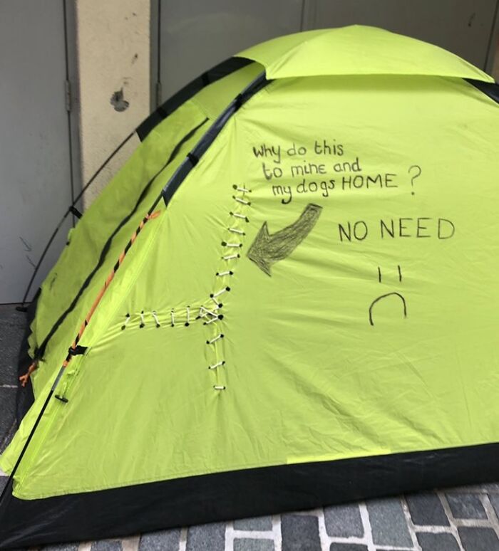 Green tent with stitched tear and handwritten message about dog home, vandalism arrow and sad face — next-level jerks