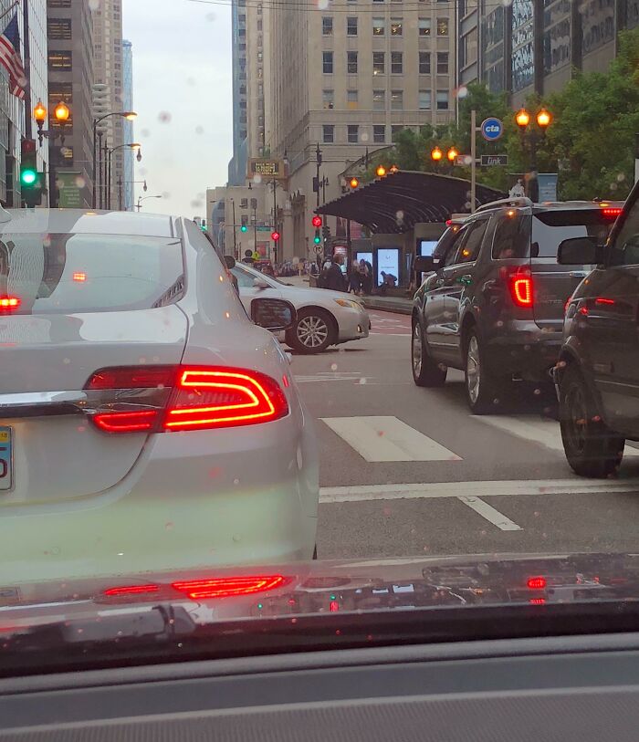 Rainy city intersection with cars blocking cross traffic, inside-car view illustrating next-level jerks.