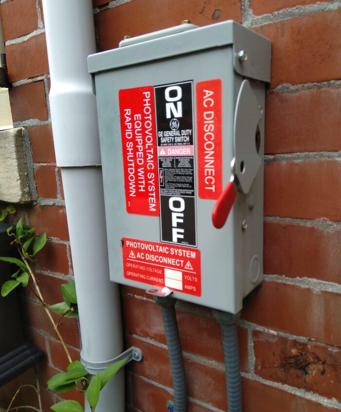 Photovoltaic AC disconnect box with red handle mounted on brick wall, next-level jerks photos