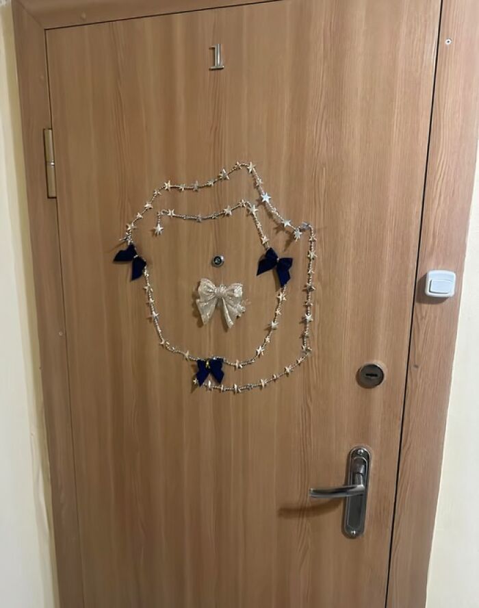 Wooden apartment door decorated with simple Christmas bows and star garland in a Lithuanian building hallway.