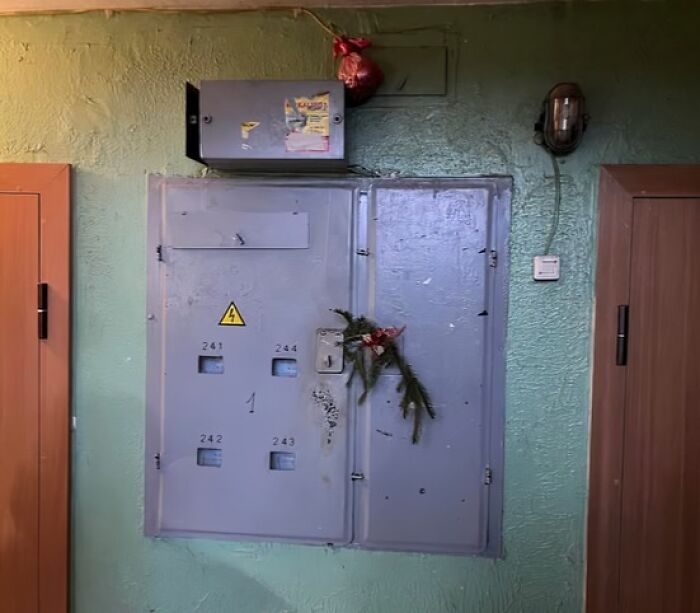 Dimly decorated Lithuanian apartment building electrical panel with minimal Christmas greenery and a small hanging ornament.