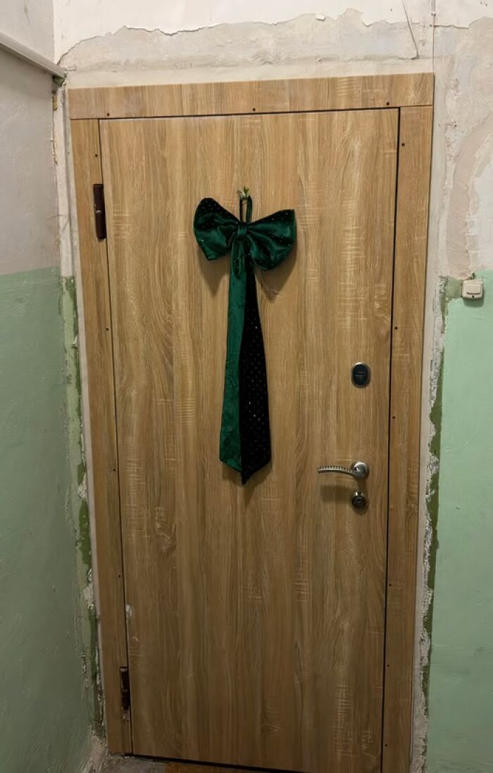 Wooden apartment door with a simple green velvet bow decoration in a worn Lithuanian building hallway for Christmas.