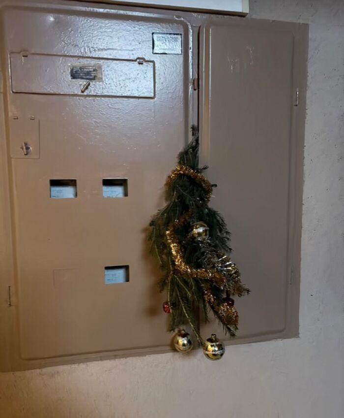 Sad apartment building Christmas decoration in Lithuania with tinsel and baubles on a utility panel door.