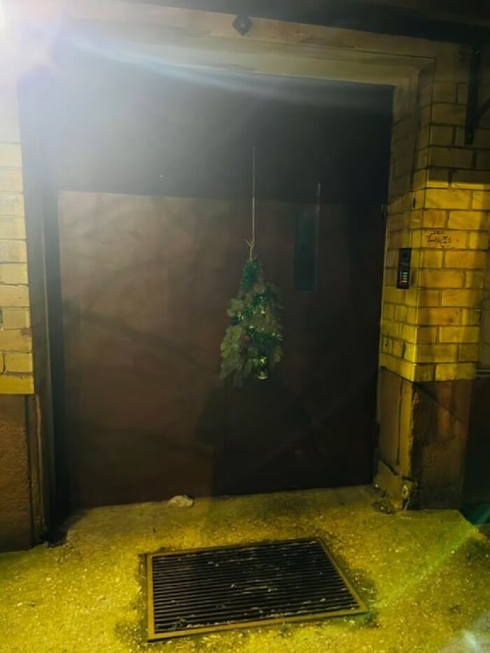 Small sparse Christmas decoration hanging on a dark door of a sad Lithuanian apartment building at night.