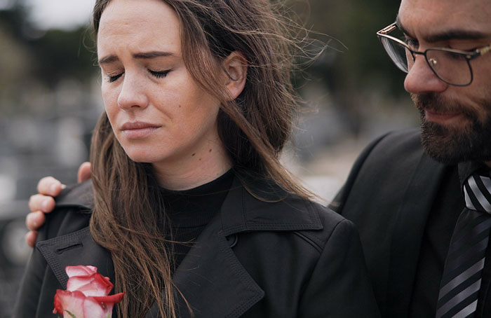 Woman grieving outdoors while a man offers comfort, representing the emotional impact of mass shooting survival tips. Woman grieving outdoors while a man offers comfort, representing the emotional impact of mass shooting survival tips.