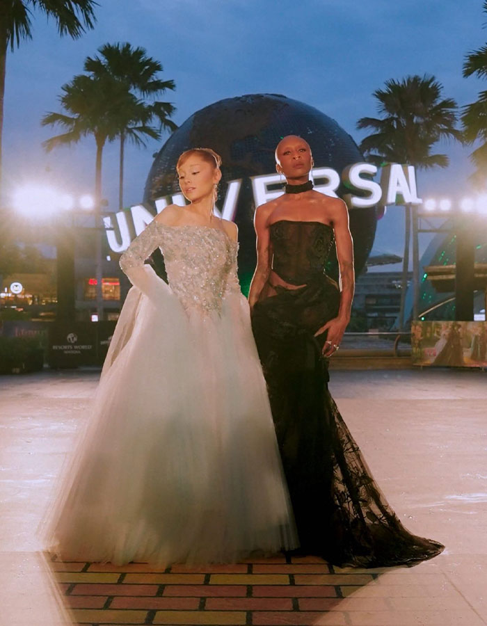 Cynthia Erivo in a striking black gown posing with a woman in a white dress at Universal Studios at dusk. Cynthia Erivo in a striking black gown posing with a woman in a white dress at Universal Studios at dusk.