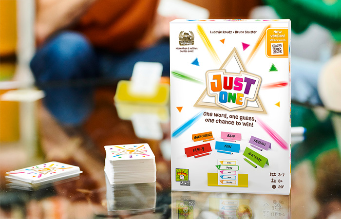 Just One party game box and cards on a table with people playing the best party game of all time.