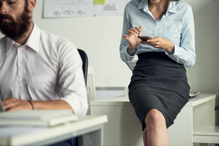 Mujer en oficina usando celular, reflejando ambiente tenso tras escándalos laborales que sacudieron el lugar de trabajo.