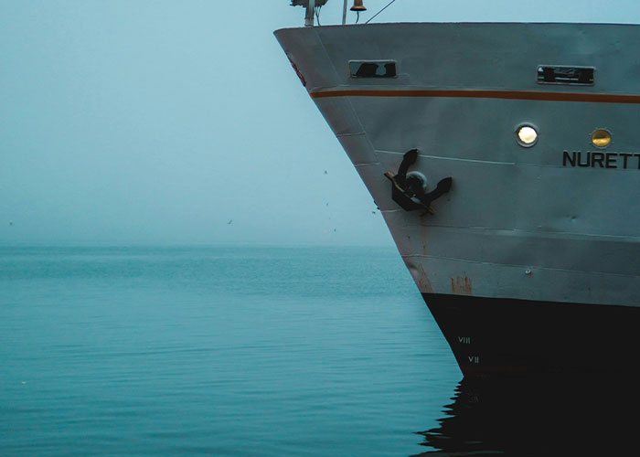 Ship's bow emerging from fog over calm water, evoking creepy and mysterious scenes in remote and isolated places.