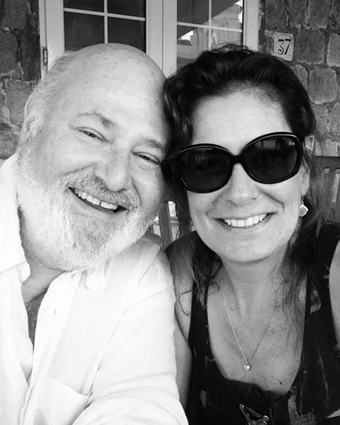 Rob Reiner smiling in a casual setting posing with a woman wearing dark sunglasses outdoors by a stone wall. Rob Reiner smiling in a casual setting posing with a woman wearing dark sunglasses outdoors by a stone wall.