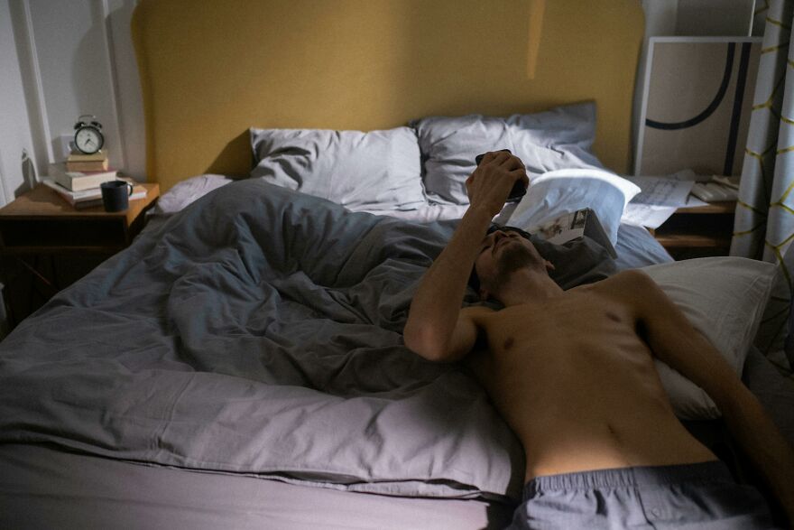 Man lying on bed in dimly lit room, looking at phone, representing good morning message to my love ideas theme. Man lying on bed in dimly lit room, looking at phone, representing good morning message to my love ideas theme.