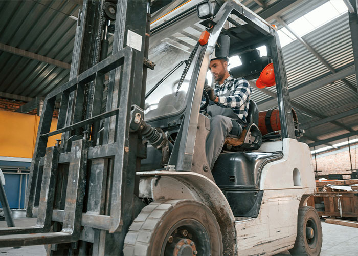 Worker operating forklift inside warehouse, highlighting safety risks and potential forklift accident hazards at worksite.