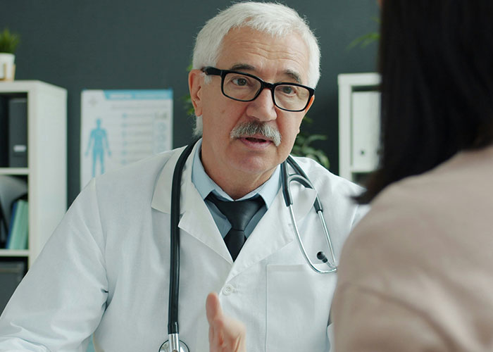 Senior doctor with glasses and stethoscope speaking to patient about unprofessional things doctors have said to patients.