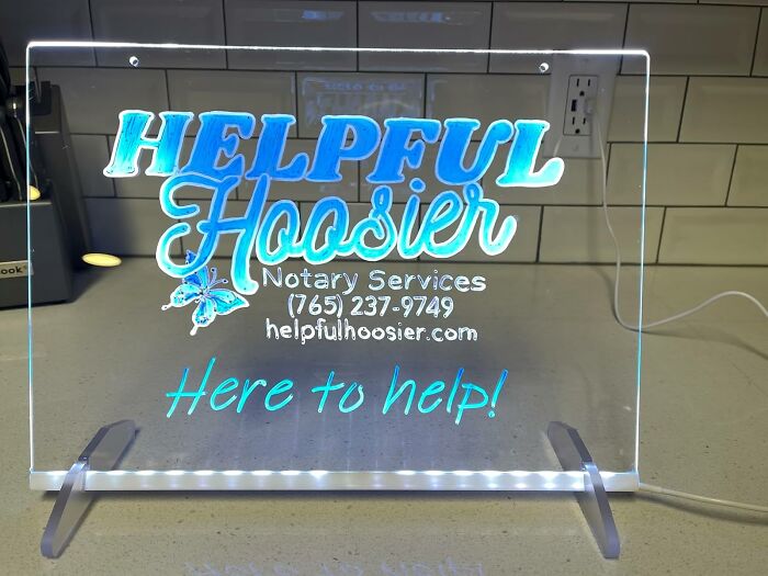 Illuminated acrylic sign for Helpful Hoosier Notary Services with contact info and tagline on a kitchen counter.