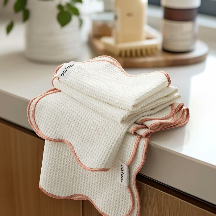 Stack of white textured kitchen towels with pink edges on a countertop, featured as unique host gifts idea