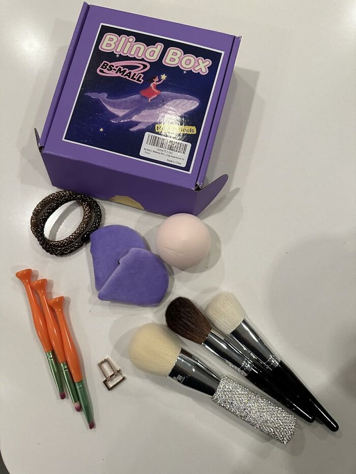 Purple blind box with various makeup tools and accessories displayed on a white surface for a game of chance.