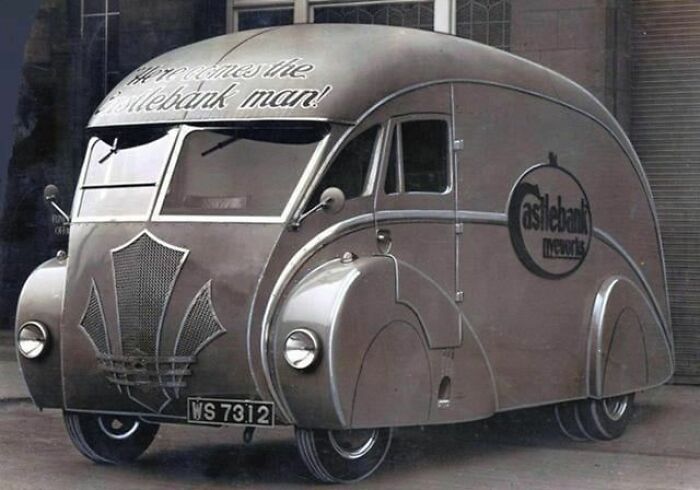 Vintage streamlined delivery vehicle parked outside a building, showcasing culture and everyday life in powerful old photos.