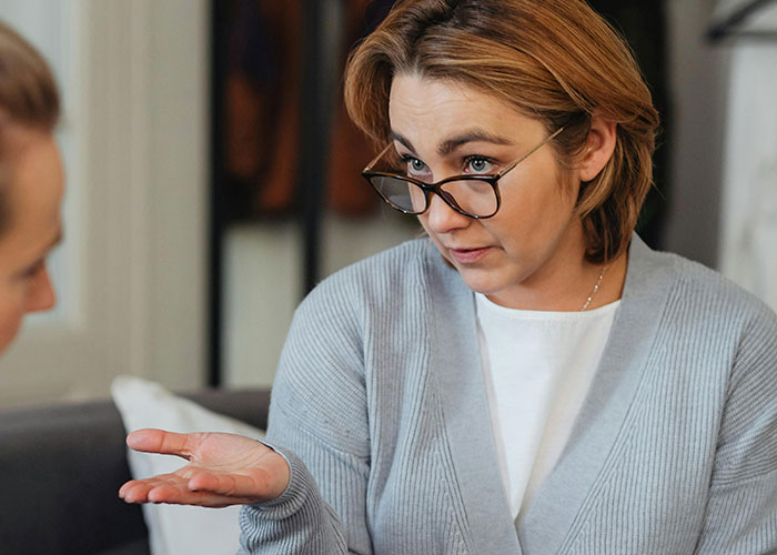 Middle-aged woman wearing glasses, gesturing with her hand during an intense conversation about unhinged things her MIL said.