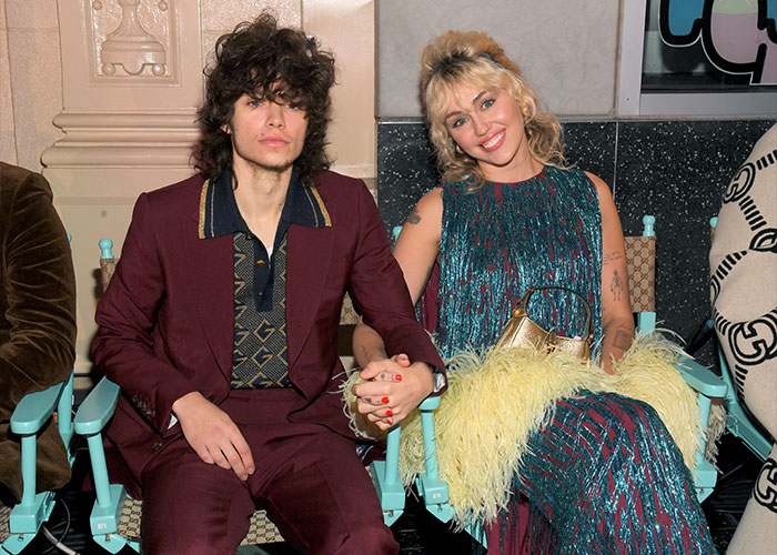 Miley Cyrus and Maxx Morando holding hands, dressed stylishly, sparking engagement and age-related reactions.