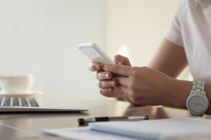Person holding smartphone near laptop and notebook, illustrating office scandals that turned workplaces upside down.