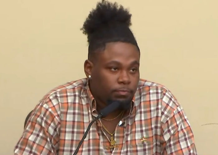 Man in plaid shirt speaking into microphone during court appearance related to beauty queen case.