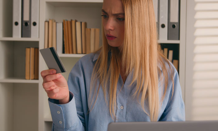 Woman looking worried holding credit card at home, representing SAHM at a loss after unexpected divorce news.