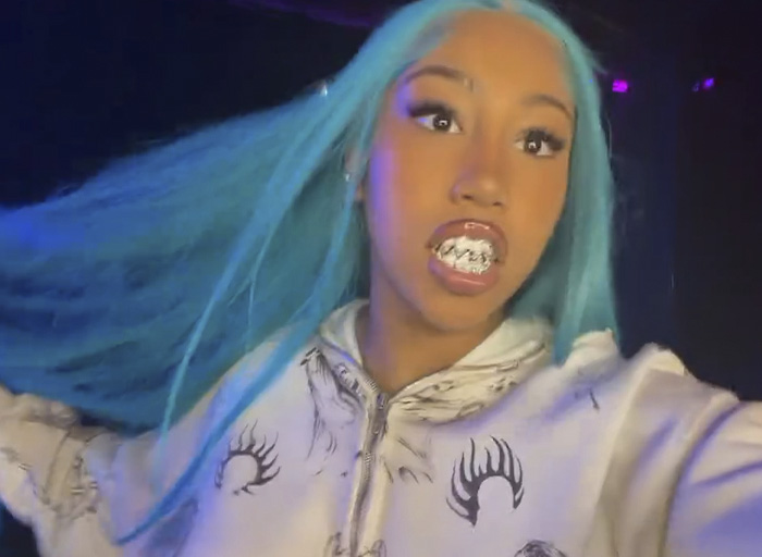 Teen with long blue hair and silver grillz wearing a graphic hoodie, sparking divided reactions on North West's new look.