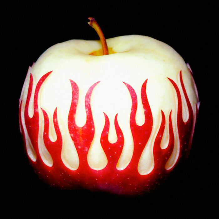 Red and white apple with flame-shaped patterns carved into the skin, creating a trippy visual effect on black background