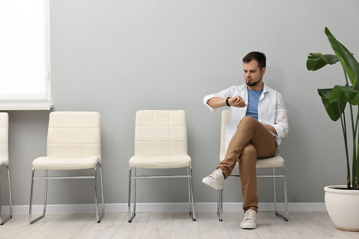 Man checking watch while waiting alone in empty room, reflecting on missed delivery of babies.