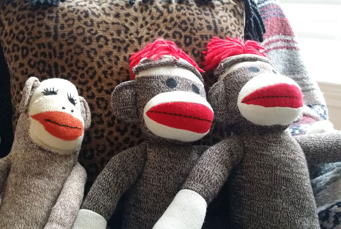 Three sock monkey dolls with red lips and hats sitting against a leopard print and striped background, white elephant gifts.