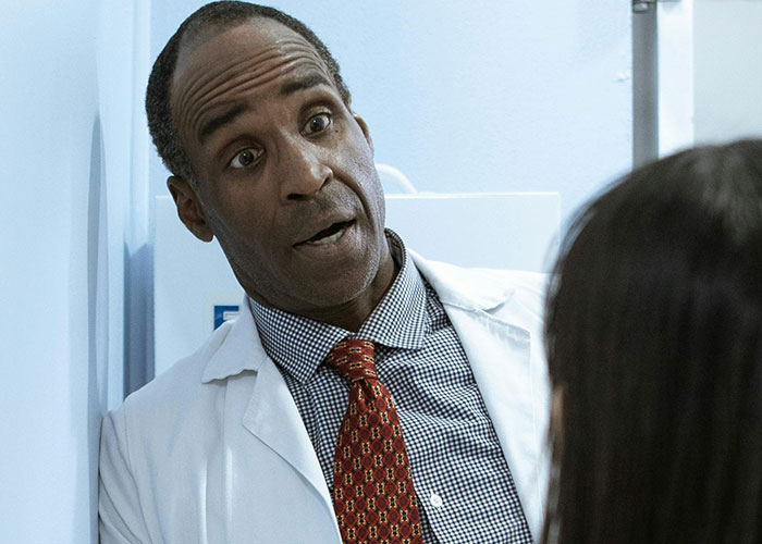 Doctor in a white coat and patterned tie speaking to a patient with an unprofessional surprised expression.