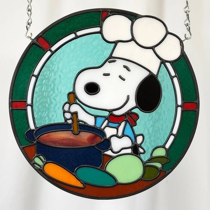 Stained glass sign of a pop culture icon Snoopy dressed as a chef stirring a pot with vegetables around.