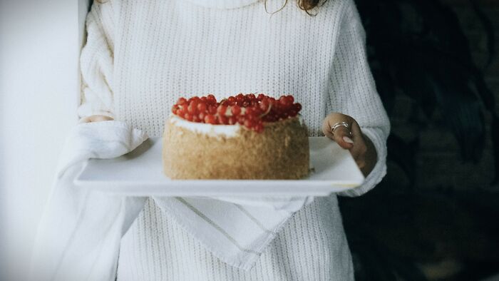 Person wearing a white sweater holding a cake on a tray, inviting you to cast your vote on ambiguous situations.