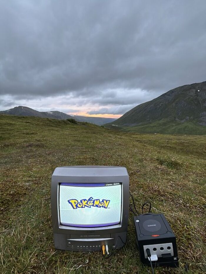 Old CRT television and GameCube on grassy hill with cloudy sky, creating a trippy picture that seems plucked from another reality