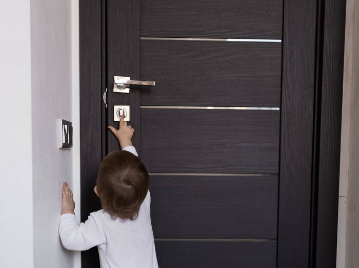Toddler reaching up to unlock a dark wooden door, illustrating a kid's insult that is strange and specific.