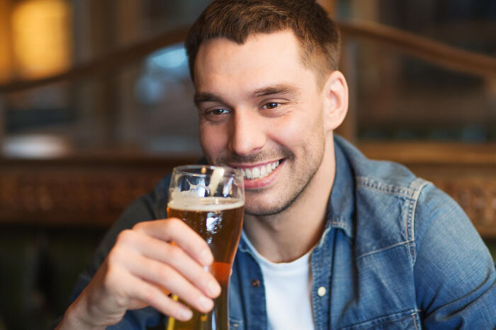 Young man smiling and holding a glass of beer, capturing a moment of strange and specific kid's insult creativity.