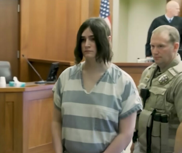 Trans Muslim woman standing in courtroom wearing striped prison uniform during sentencing hearing with law enforcement officers nearby Trans Muslim woman standing in courtroom wearing striped prison uniform during sentencing hearing with law enforcement officers nearby