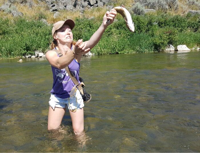 Woman in river awkwardly throwing a fish, a funny and interesting weird pic taken at the perfect time.