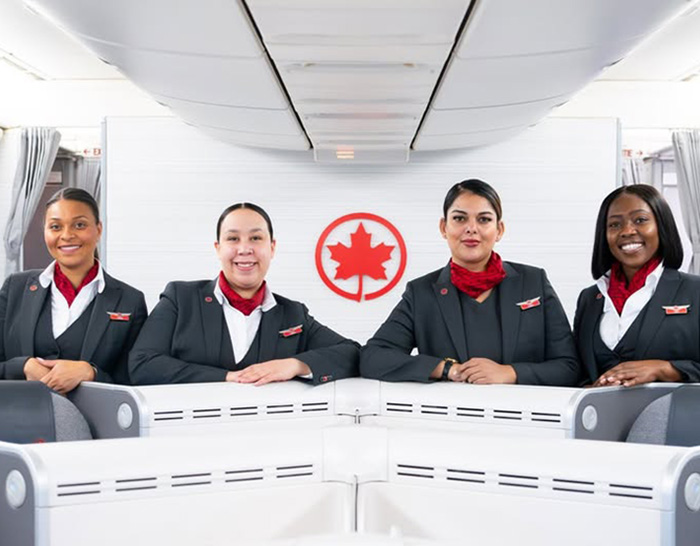 Cuatro auxiliares de vuelo de Air Canada dentro de la cabina del avi&oacute;n con el logo visible detr&aacute;s.