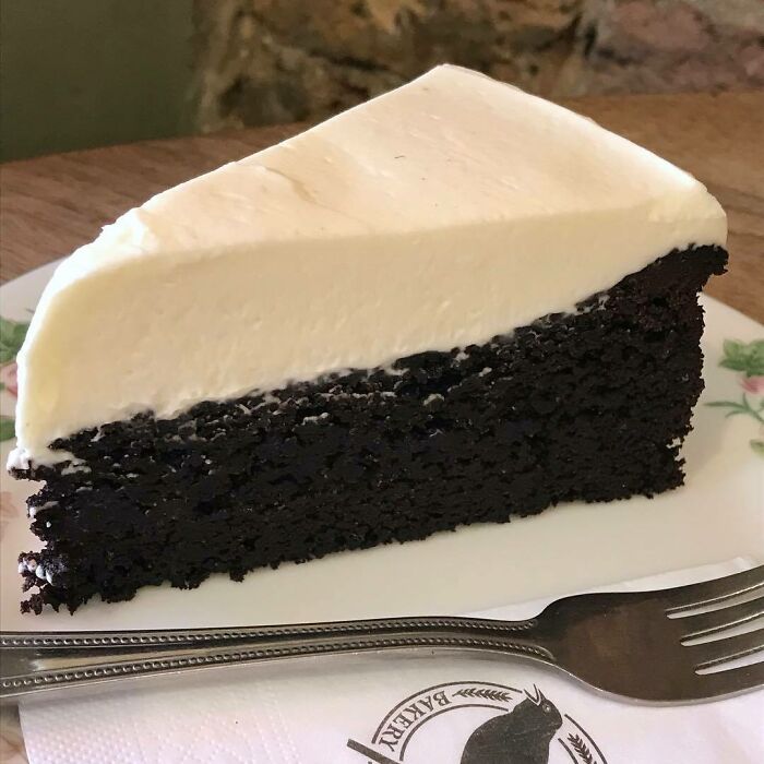 Slice of rich chocolate cake with creamy white frosting on a plate, showcasing a delicious Christmas dessert from around the world.