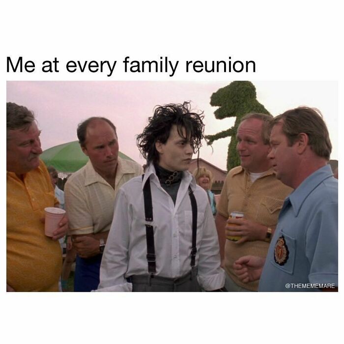 Person dressed in goth style standing awkwardly among casually dressed people at an outdoor family reunion gathering.